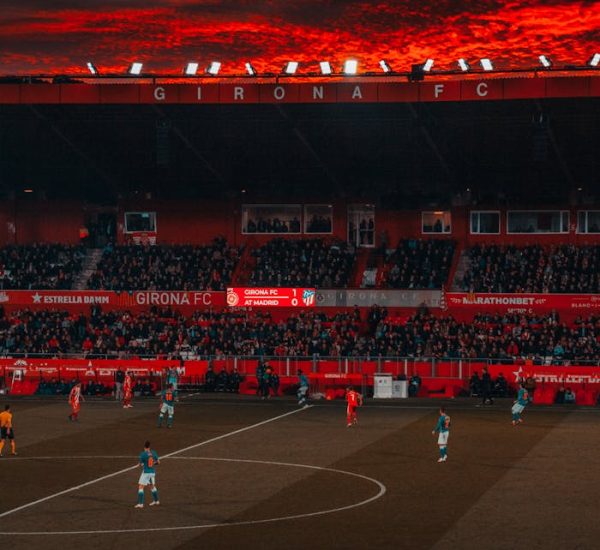 Dramatic evening soccer game at Girona FC stadium with vibrant red sky and intense play.