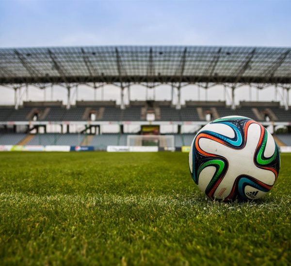 Close-up of a soccer ball on a lush grass field with an empty stadium in the background.